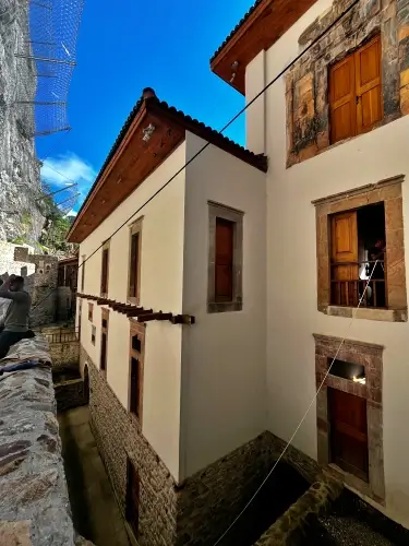 Trabzon Sümela Manastırı’nda Osmanlı döneminde yenilenen keşiş hücreleri ve konaklama yapıları; beyaz sıvalı üst katlar, ahşap pencereler ve kayalık yamaca yaslanan mimari detaylarıyla birlikte görünüm.